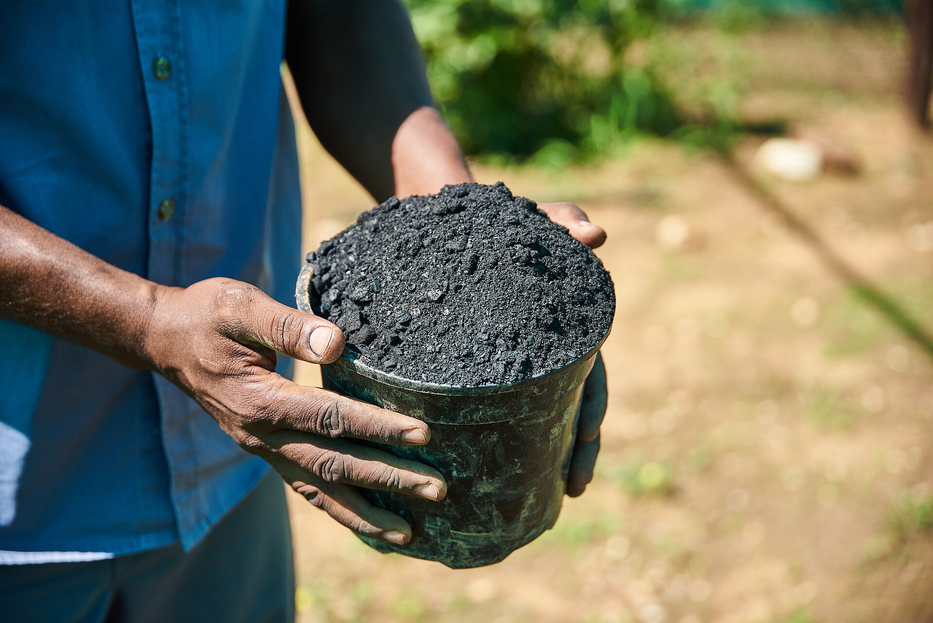 A hand holding a finished biochar briquette ready for soil
