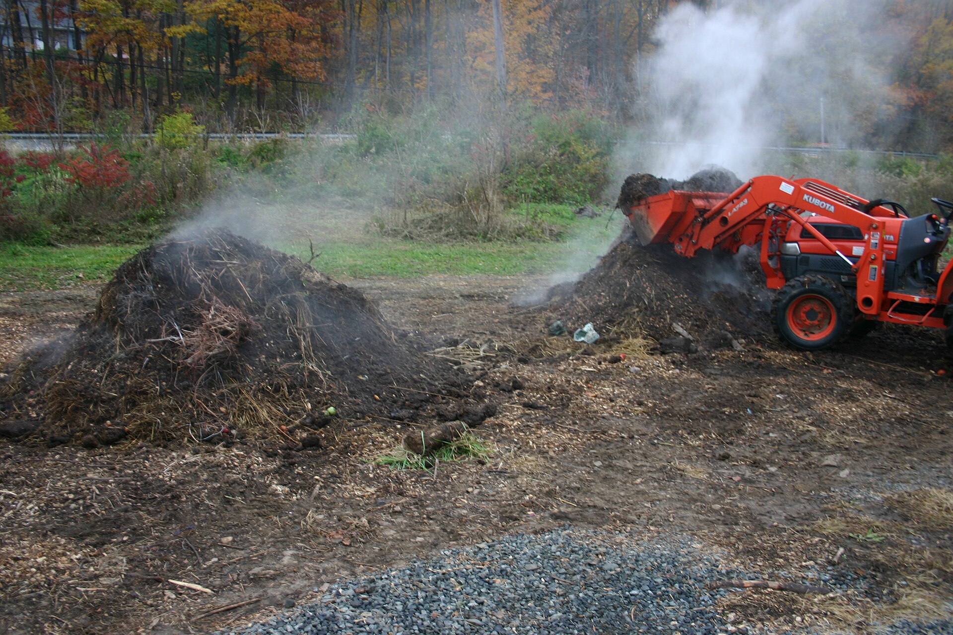 A steaming hot compost pile being turned with a machine